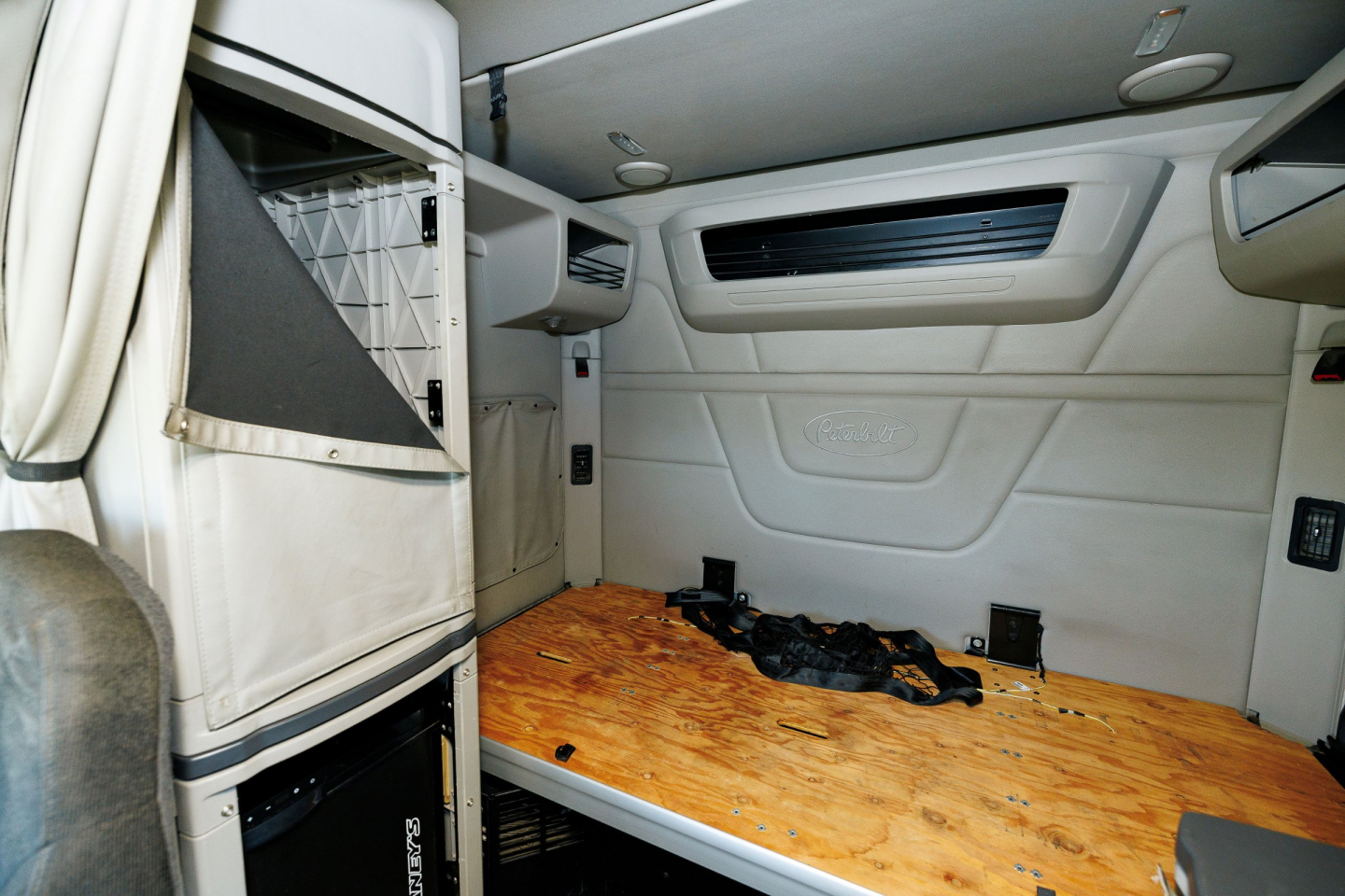 Peterbilt 579 sleeper cab interior cargo area with wooden floor and side storage, showing upper bunk and window panel.