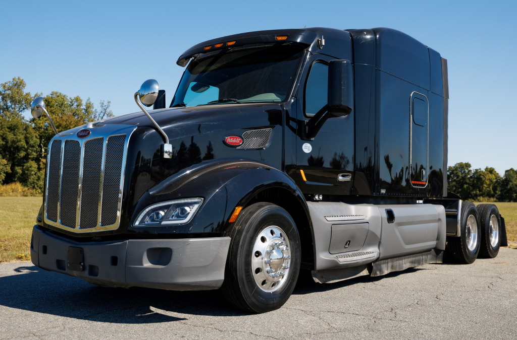 Peterbilt 579 conventional sleeper truck in dark blue, front-left view showing chrome grille, bumper, and side step.