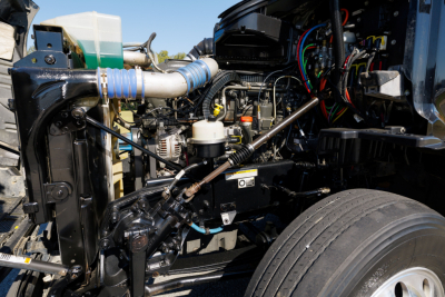 Peterbilt 579 engine bay with visible hoses, wiring, and coolant reservoir; front wheel and chassis components visible
