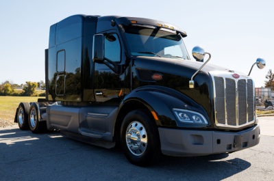 Peterbilt 579 tractor in-service black sleeper cab with chrome grille and dual rear axles showing exterior front and side view.