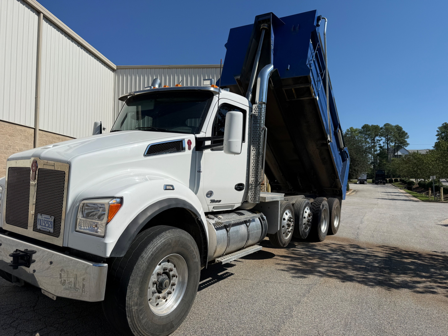 Kenworth T880 dump truck with blue dump body raised, white cab, side view showing front grille and dual rear axles.