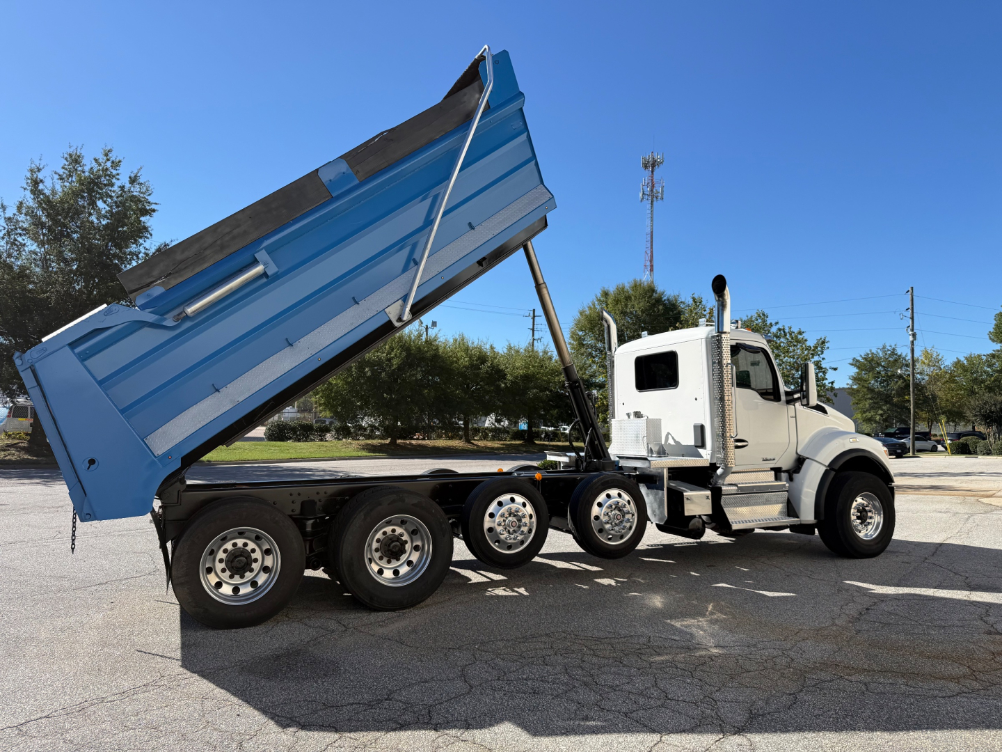 Kenworth T880 dump truck with a raised blue dump bed and white cab, multiple rear axles, side view showing the chassis and hydraulic lift.