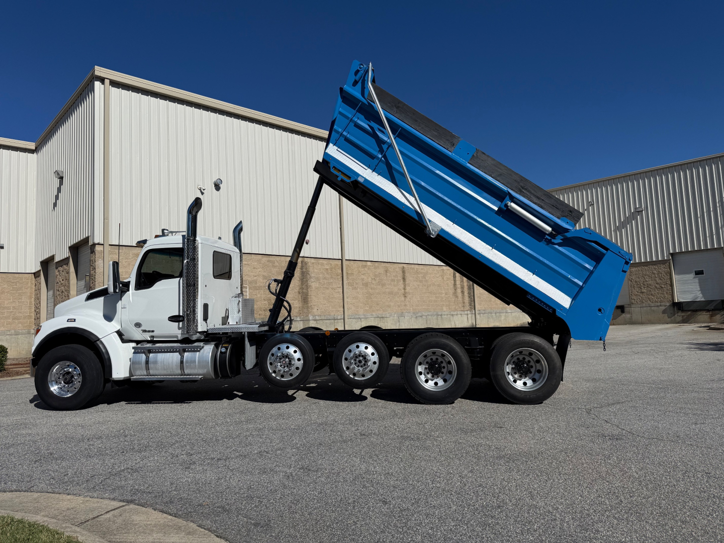 Kenworth T880 dump truck in-service showing white cab and blue dump bed with multiple axles in a parking lot.