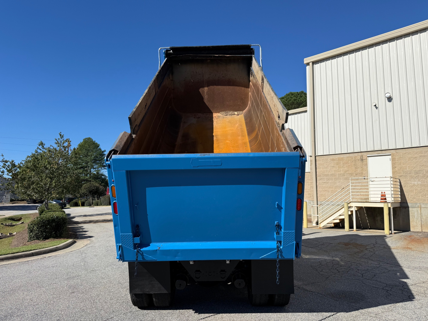 Dump truck bed of a 2022 Kenworth T880 dumping load with blue tailgate and orange interior, viewed from rear.