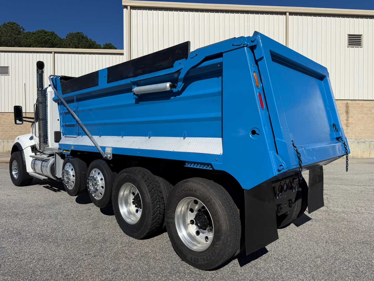 Kenworth T880 dump truck side view showing blue dump body and multiple rear axles.