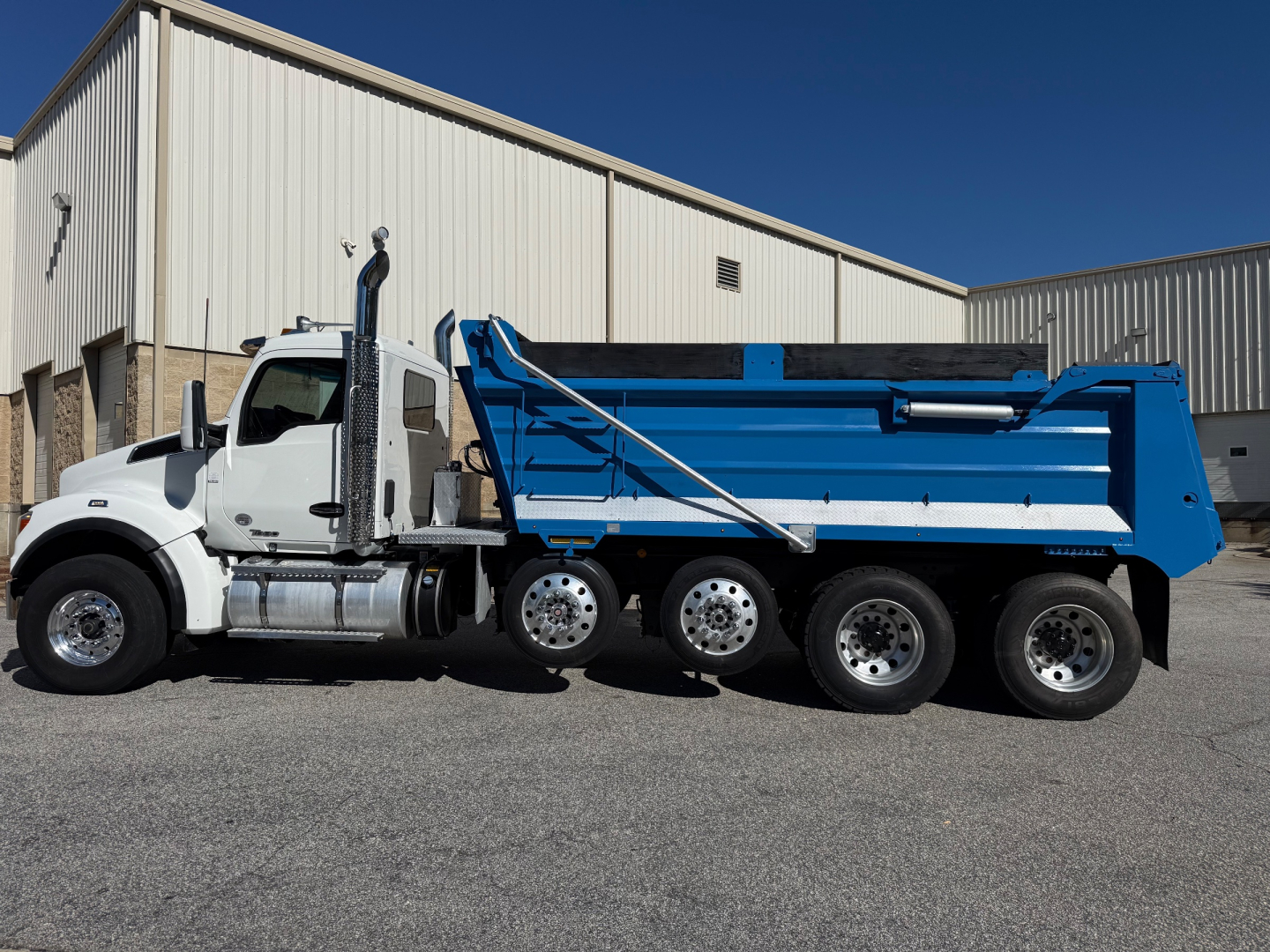 Kenworth T880 dump truck side view showing blue dump body and white cab with chrome fuel tanks and black tires.