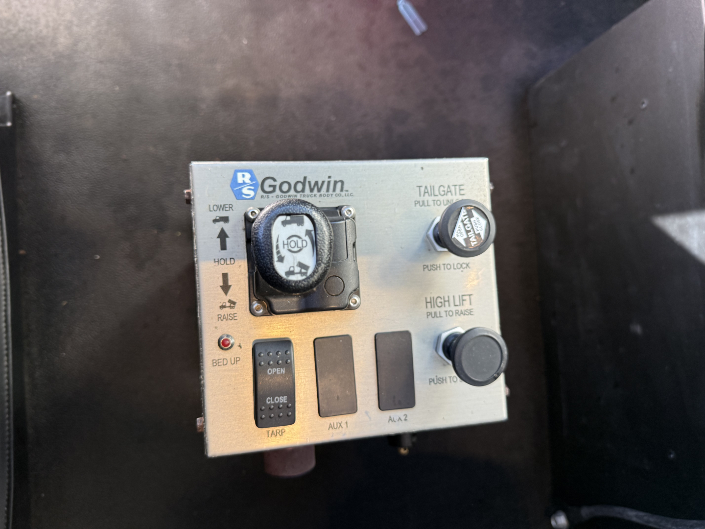 Kenworth truck dash view showing Godwin tailgate control panel with knobs and labels including ‘TAILGATE’, ‘LOWER’, ‘RAISE’, and ‘HIGH LIFT’ along with auxiliary switches.