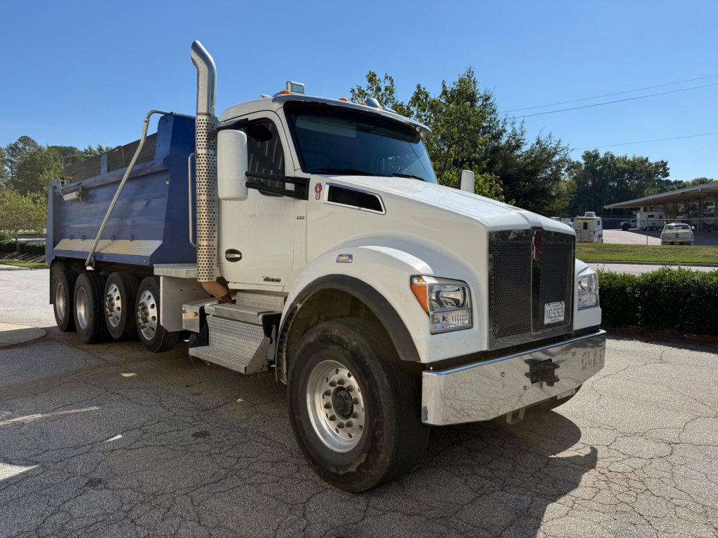 Kenworth T880 dump truck with white cab and blue dump bed, side view, showing large chrome exhaust stacks, dual rear wheels, and chrome bumper.
