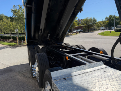 Truck chassis and dump bed section of a 2022 Kenworth T880 showing dual rear axles, hydraulic dump mechanism, and diamond plate step.