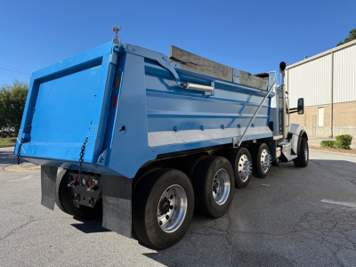 Kenworth T880 dump truck rear and side view showing blue dump bed and triple rear axles