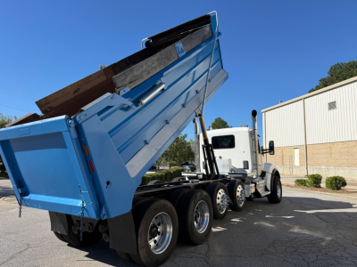 Kenworth T880 dump truck in raised bed showing side view and rear dual axles with blue dump body.