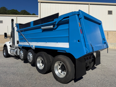 Kenworth T880 dump truck side view showing blue dump body and multiple rear axles.