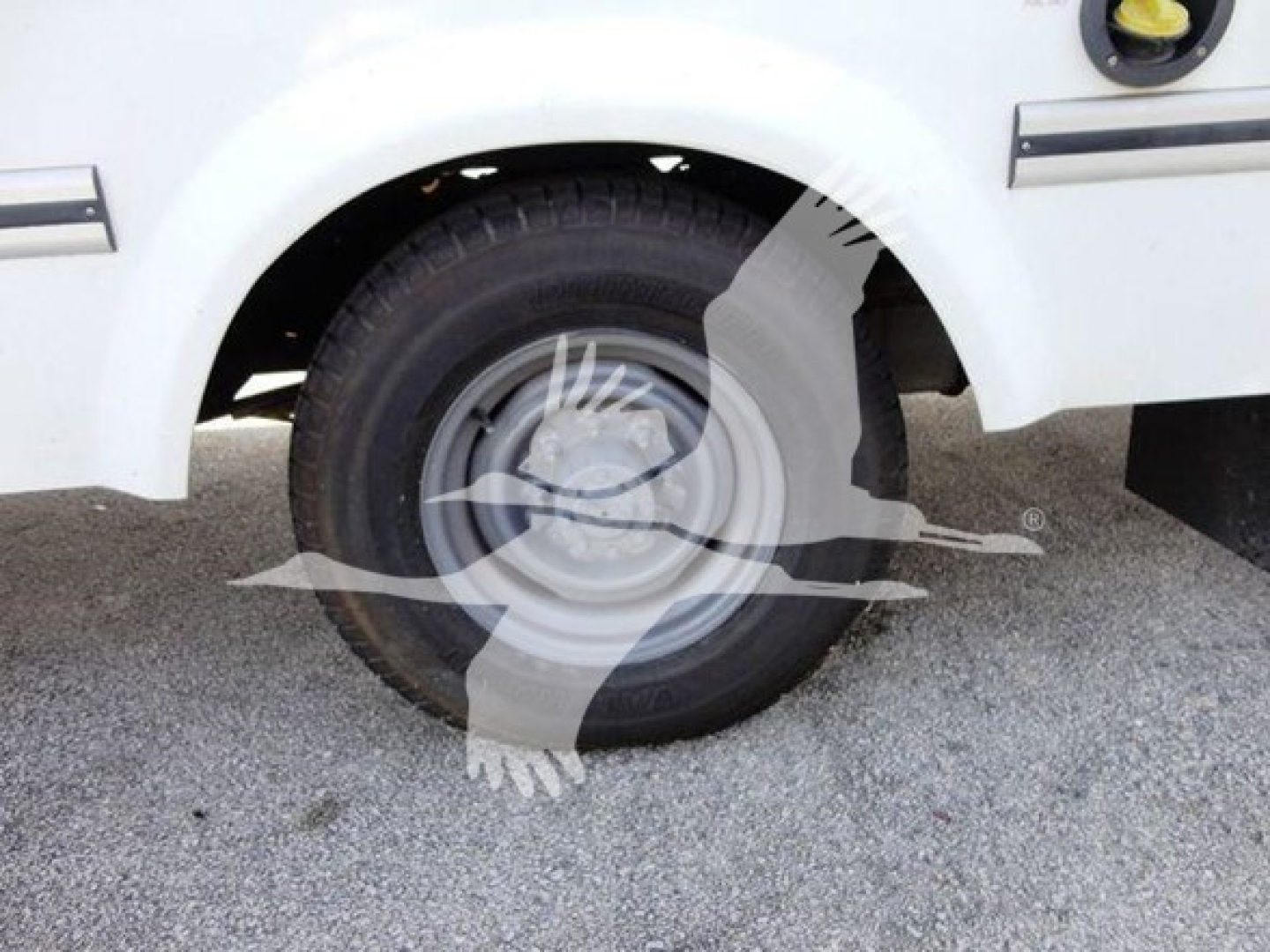 Ford E-Series van/box truck front wheel well and tire in view showing white body and wheel.