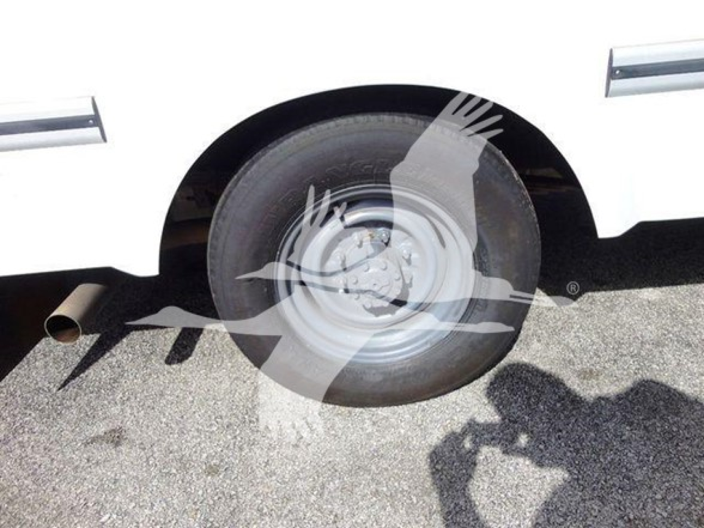 Front wheel area of a white Ford E-350 Cutaway/High Cube showing wheel, exhaust, and side panel; no legible labels visible.