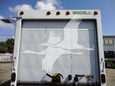 Back of a white Ford E-350 cutaway with a decorative seagull decal on the liftgate, emergency lights at top, and corner hinges.