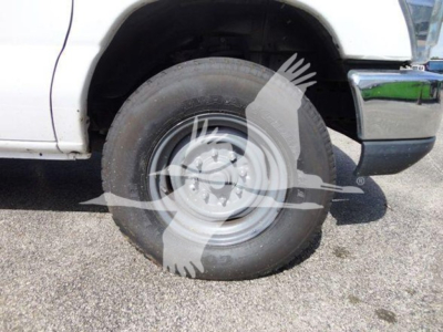 Front wheel and fender of a white 2015 Ford E350 SD cutaway truck showing wheel and tire with wheel well; no legible model text visible on the image.