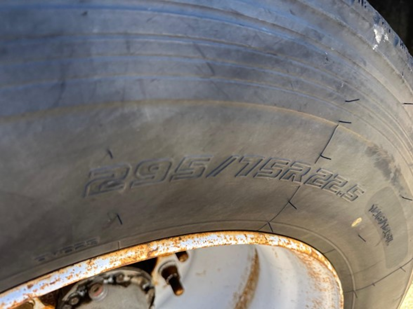Tire sidewall showing 295/? inch tire with rusted wheel well edge on a utility trailer.