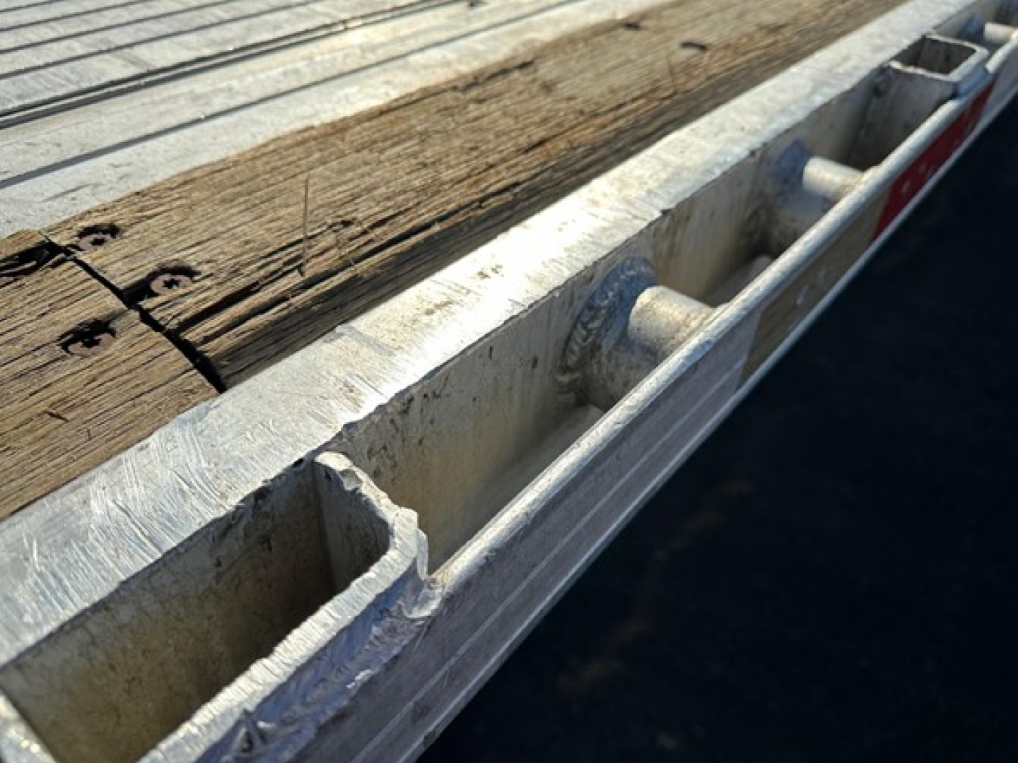 Utility trailer edge with wooden deck and metal stake pockets visible.