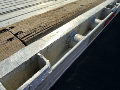 Utility trailer edge with wooden deck and metal stake pockets visible.