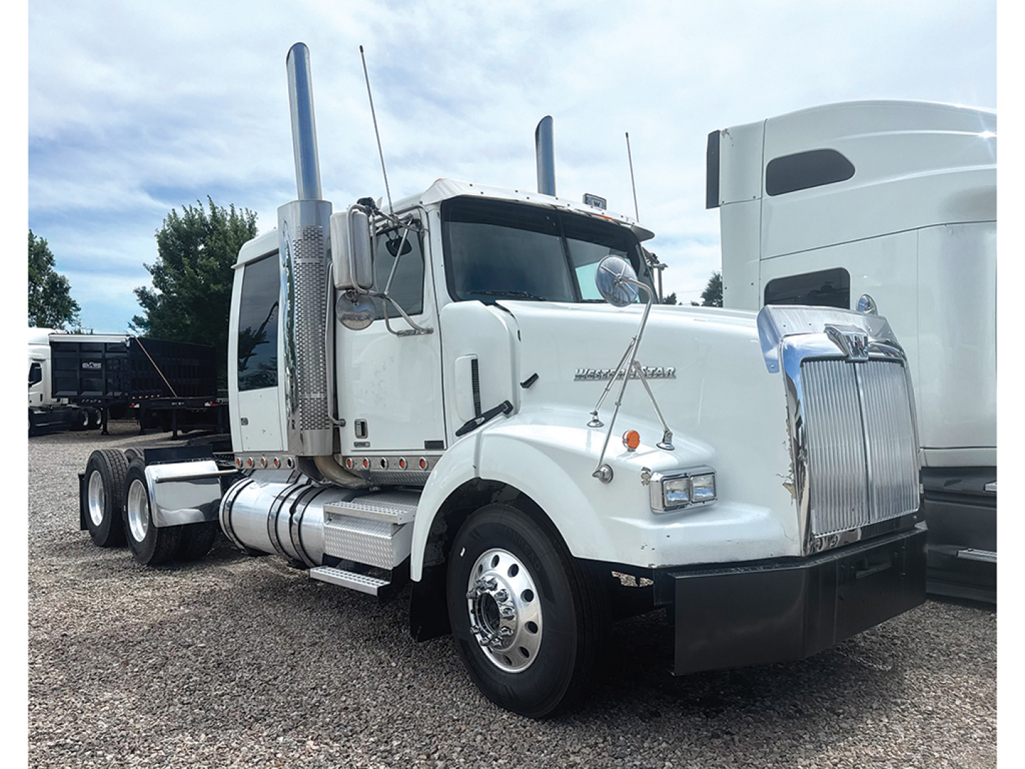 White Western Star 4900SB heavy-duty truck with chrome exhaust stacks, dual rear axles, and large grille. visible text on side reads 'western star' and there are vertical exhaust pipes.