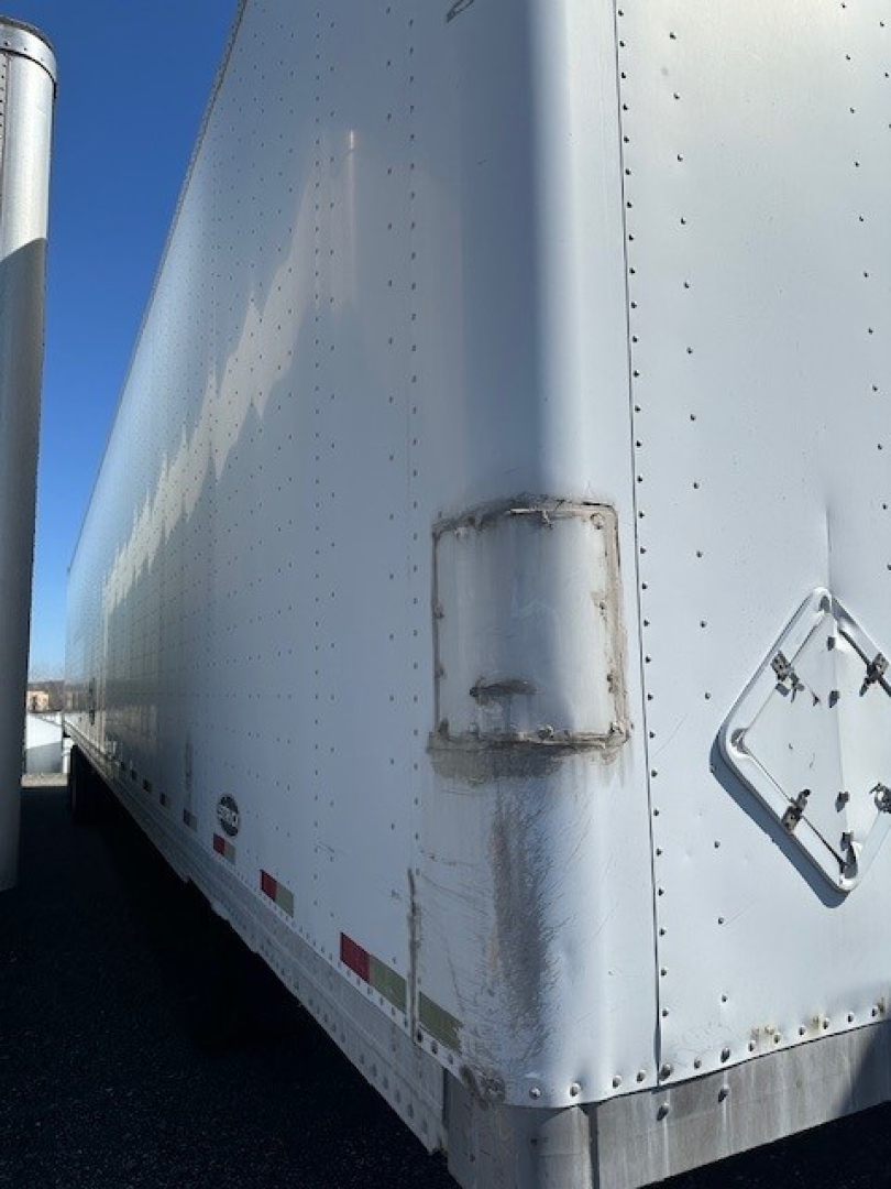 Trailer side panel with a rectangular access hatch and riveted aluminum skin; corner edge and lower trim show minor surface wear and welded seams.