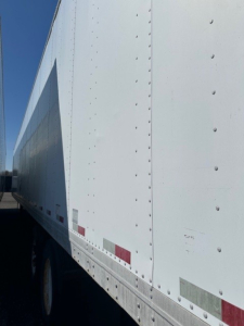 Trailer side of a 2007 Strick roll door trailer showing riveted white aluminum siding and reflective safety stripes.