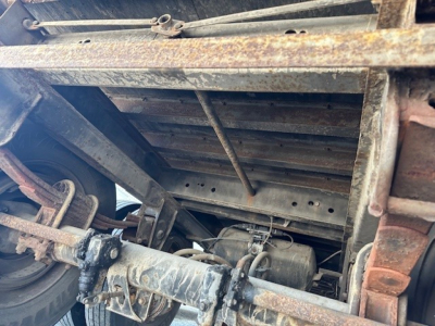 Trailer components showing underside of 2007 Strick Roll Door trailer with rusty frame, axle, and drive shaft visible; mechanical linkages and mounting brackets.