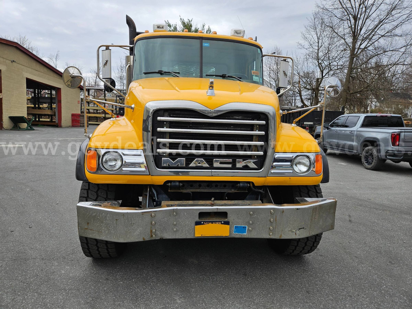 Front view of a yellow 2005 Mack CV713 flatbed truck showing large chrome grille, Mack emblem, headlights, and bumper.