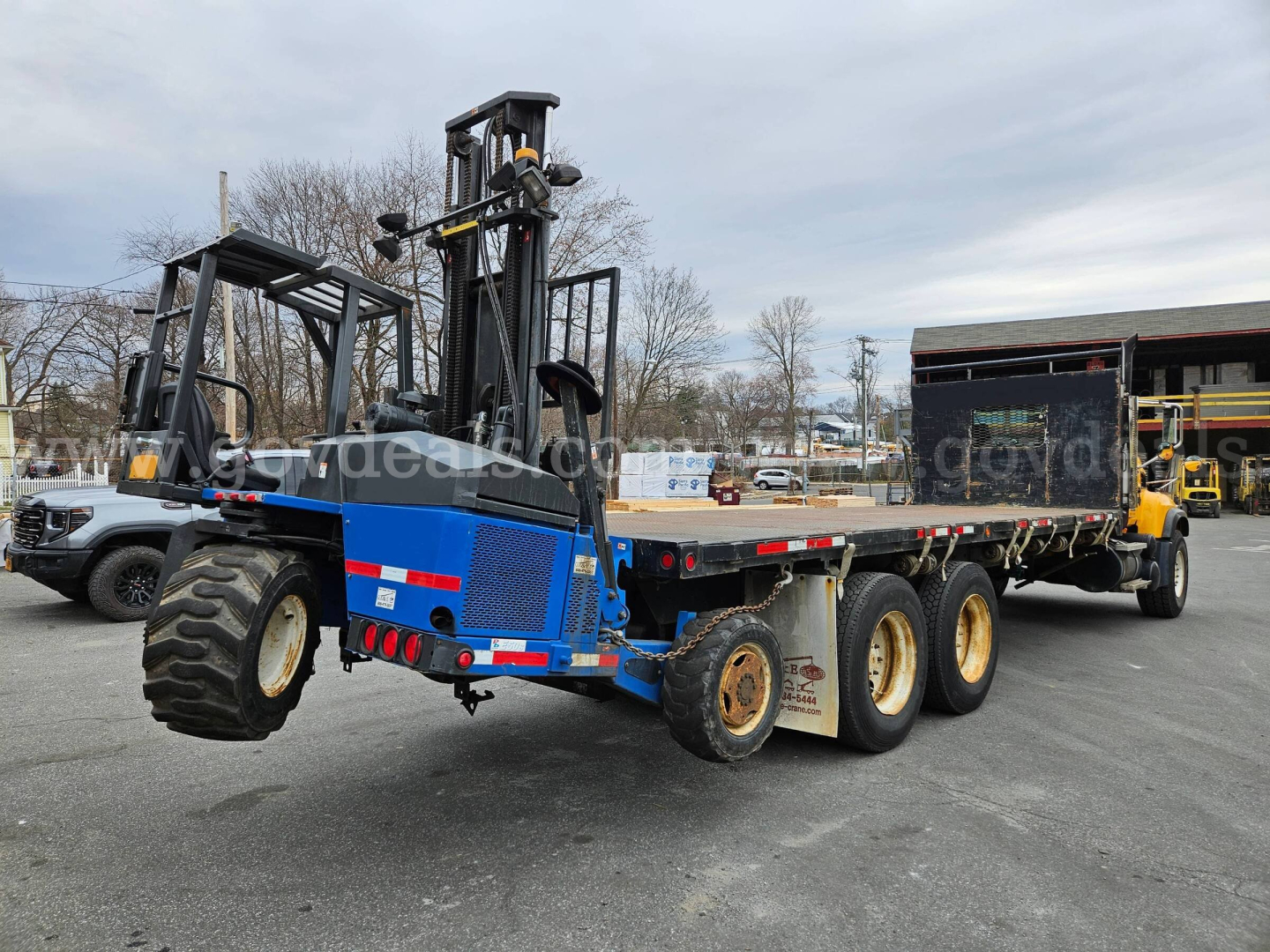Mack CV713 flatbed truck with blue lifting equipment and multiple axles, side view showing trailer and rear tires.