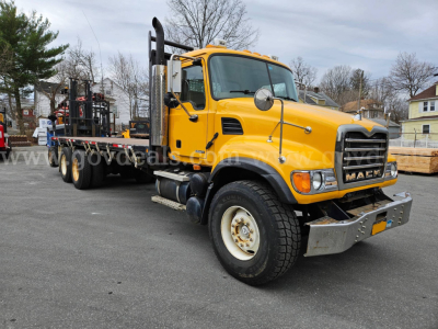 Yellow 2005 Mack CV713 flatbed truck in a lot with a long flatbed trailer attached, front view showing grille and headlights.