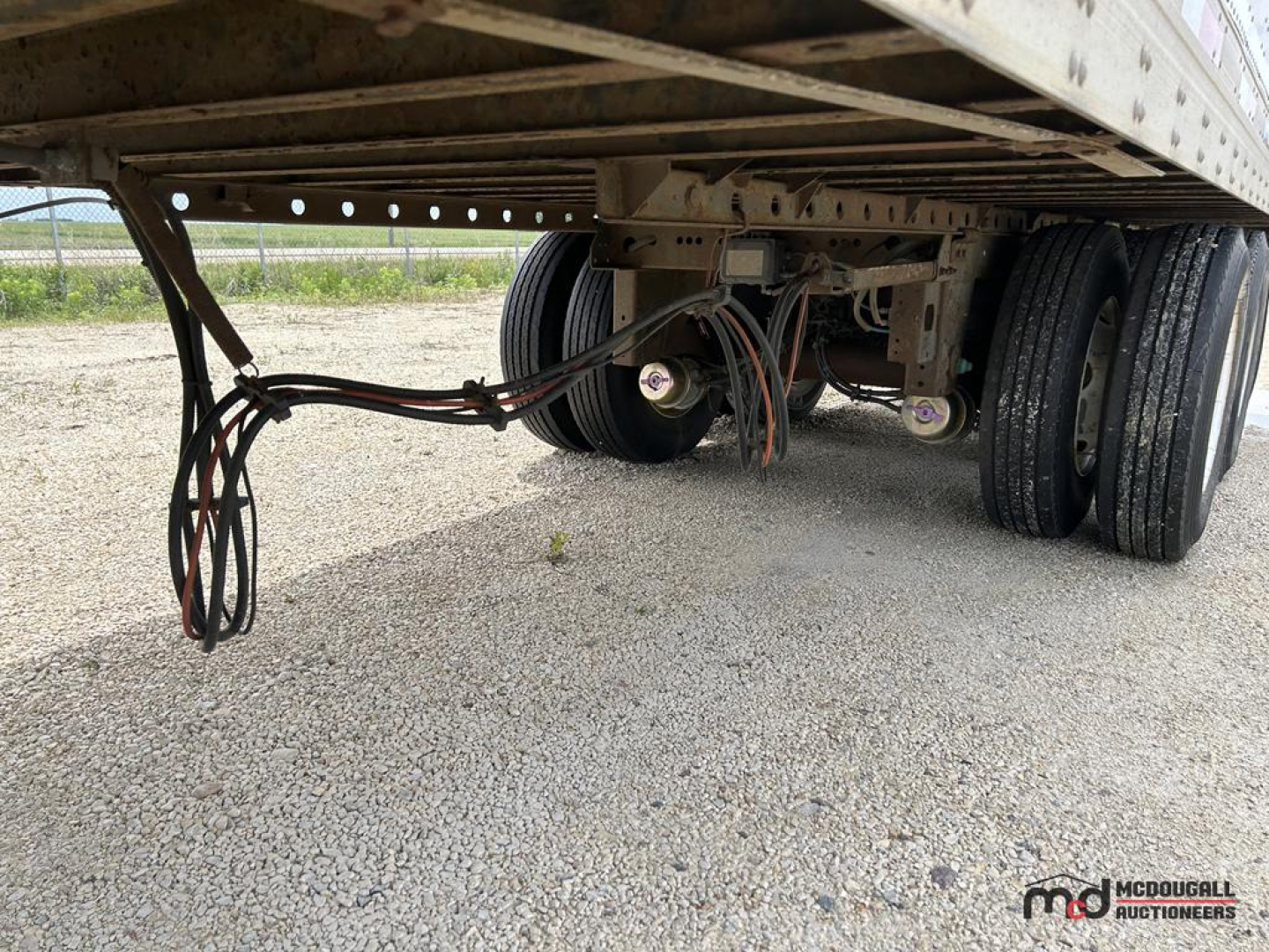 Trailer underside showing dual rear axles and wiring harness under a dry van trailer, with wheels and frame visible.