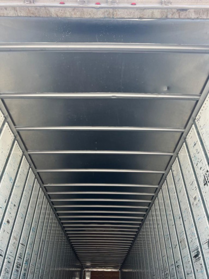 Trailer interior showing vertical corrugated walls and overhead support rails from van trailer.