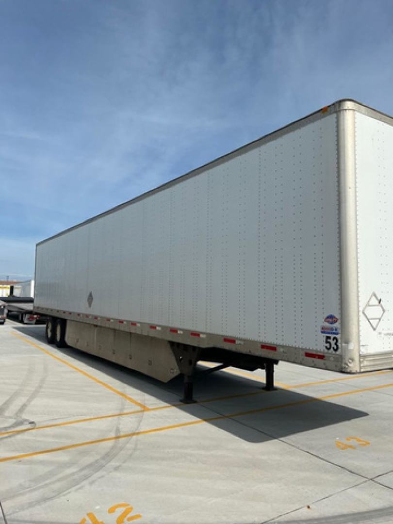 Trailer van body with overhead view showing side of a white semi-trailer container, DOT placards and wheel area in a parking lot.