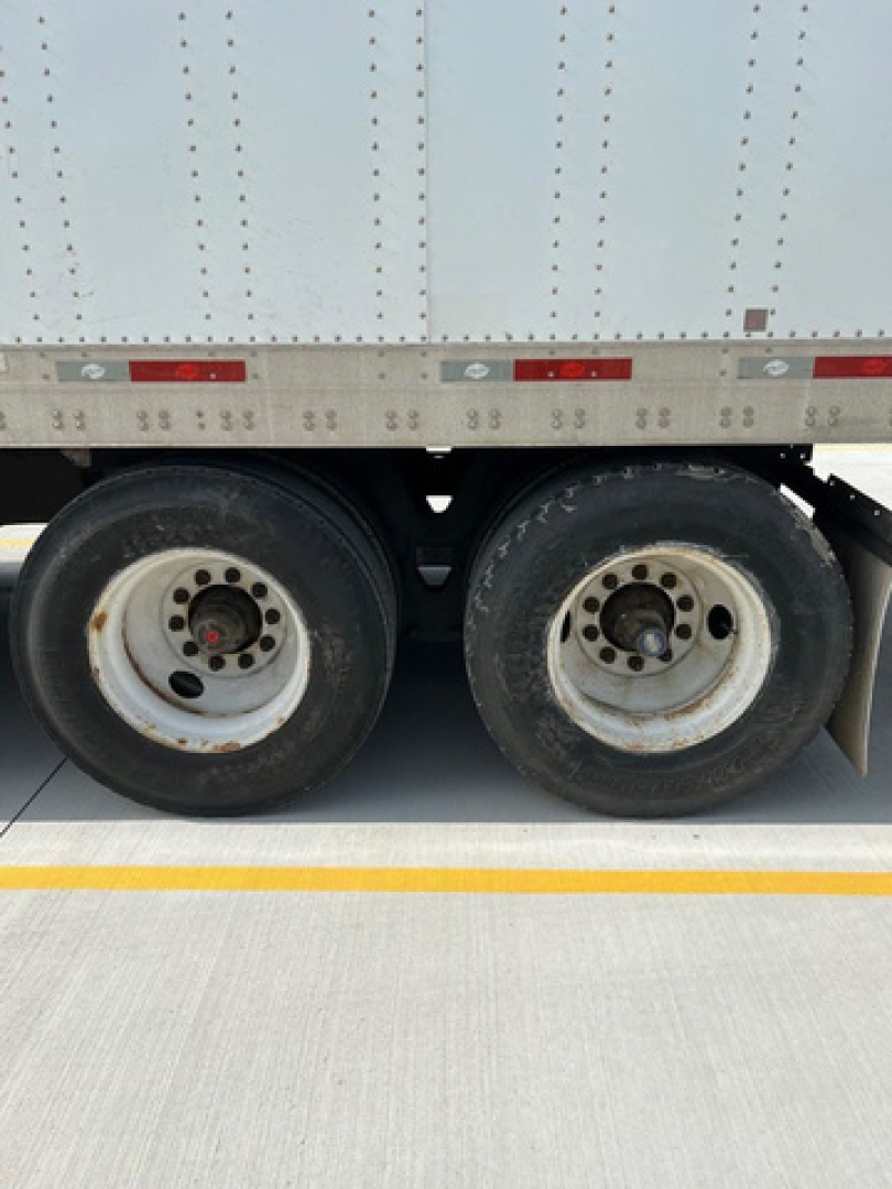 Trailer wheel area of a used 2011 utility van with dual rear axles, showing rims and tires, side of cargo box, with some reflective markings.
