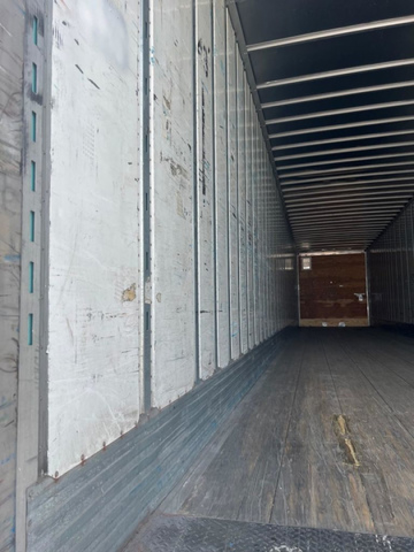 Interior of a trailer van showing metal wall panels and wooden floor, empty cargo area.