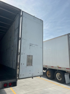 Truck trailer rear door open showing empty cargo area of a used 2011 utility van with another trailer in background.