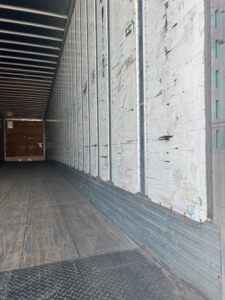 Interior of a used utility van trailer showing metal side walls, wooden floor, and open rear with load area.