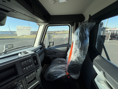 Cab interior of a 2027 Mack AN64T daycab truck showing the driver seat with plastic covering and dashboard controls.