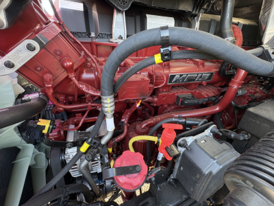 Mack AN64T engine bay showing red engine block with MHP badge, hoses, battery, and radiator components.