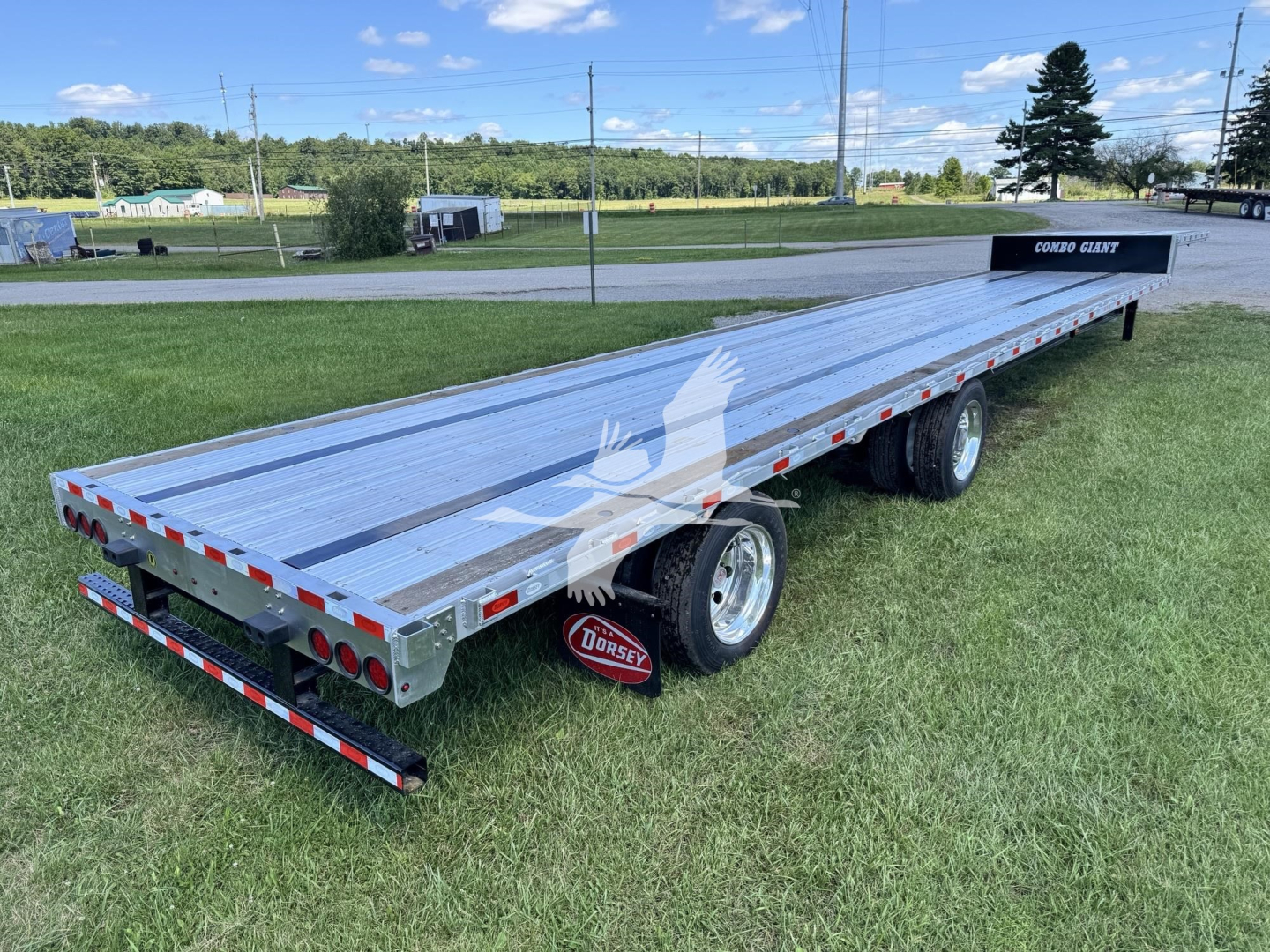 Flatbed trailer showing dual rear wheels and metal deck with red/white safety reflectors; 'Combo Slant' side rail label visible near back.