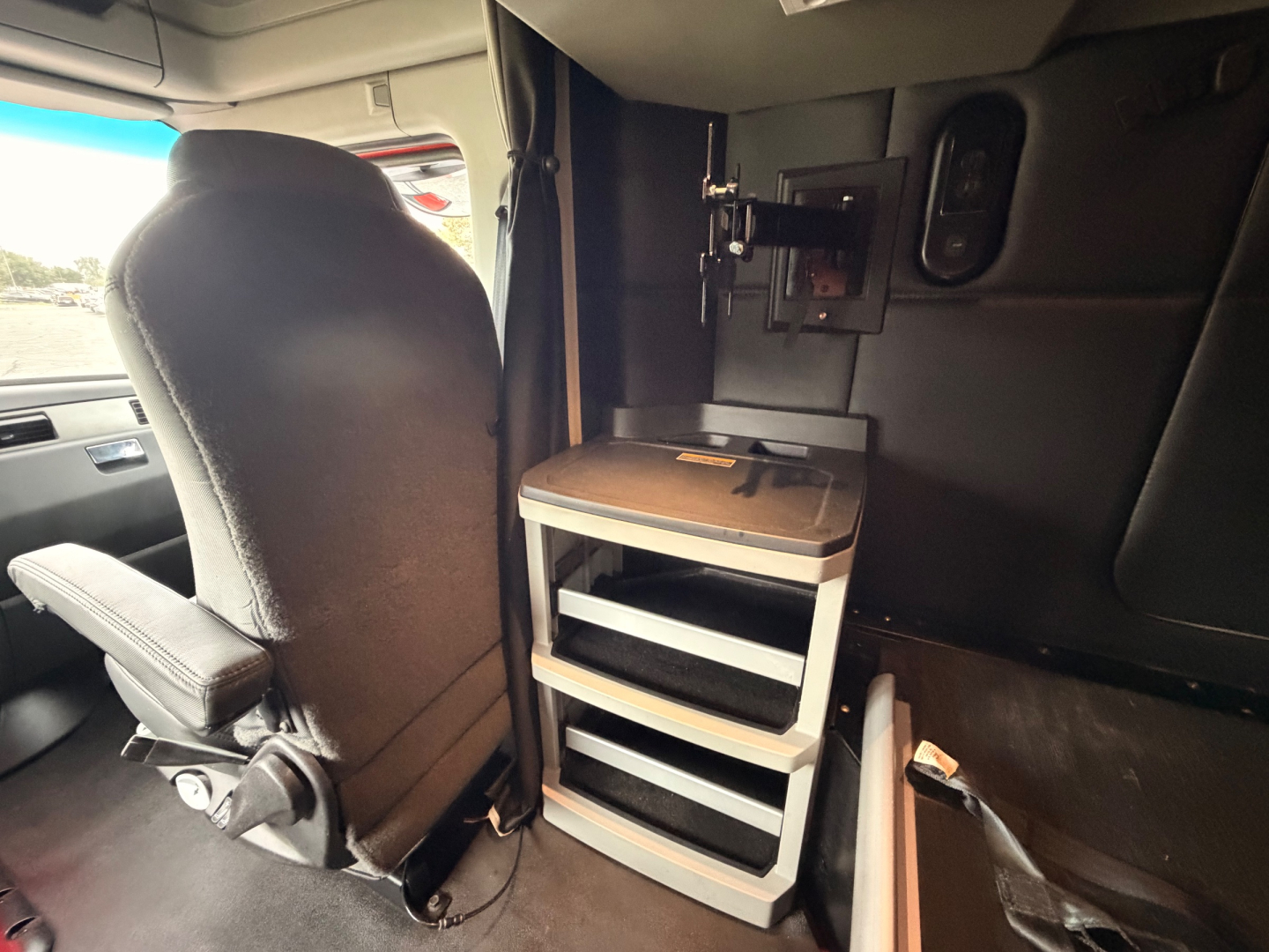 Kenworth T680 interior showing driver seat, dashboard, and side cabinet with drawers; vertical storage unit with shelves in cab.