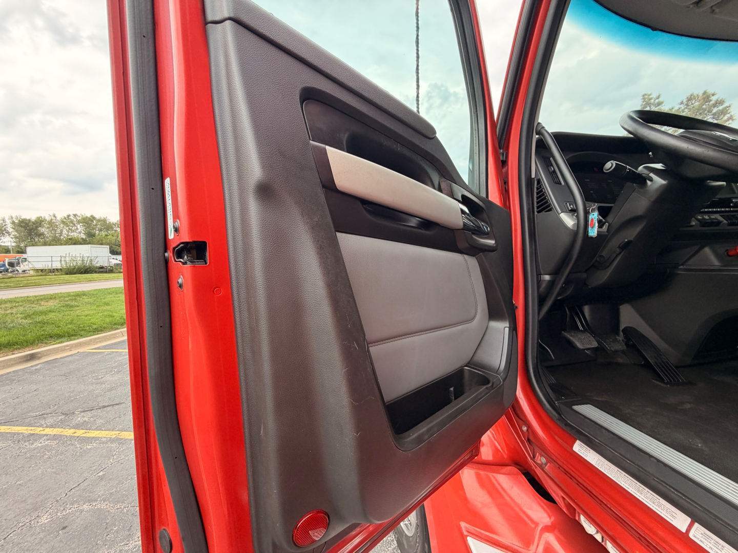 Door interior view of a red Kenworth T680 cab showing front door panel and dashboard area, with partial steering wheel visible.