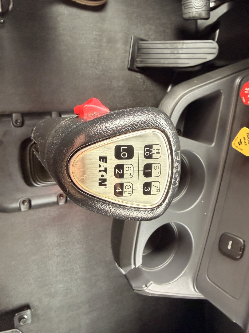 Truck interior showing a gear shifter with P R N D 2 1 labeled 'EATN' and ignition area; pedal visible; circular cup holders and dashboard controls.