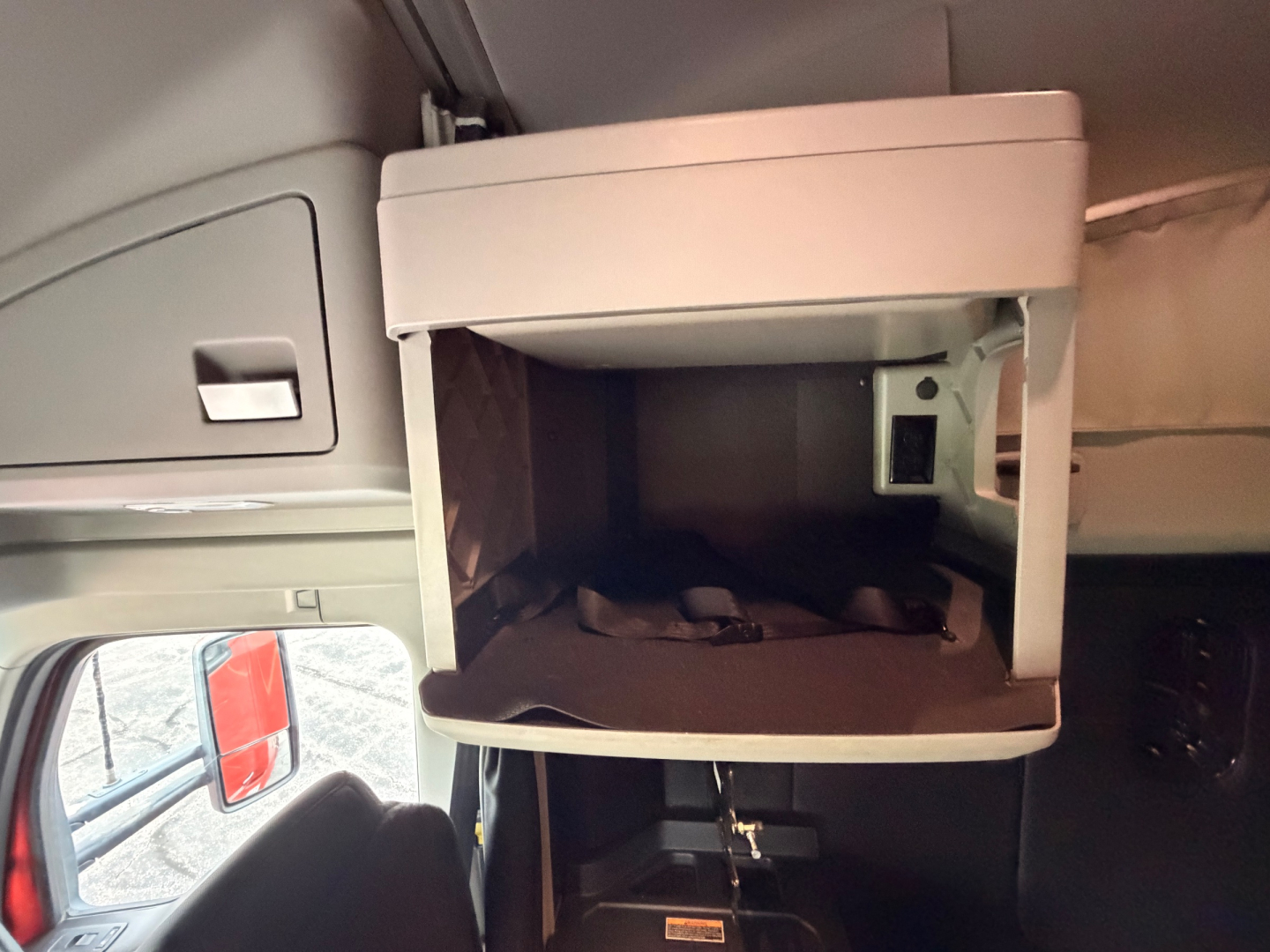 Kenworth truck interior showing overhead sleeper compartment with open storage shelf and small cubby; dashboard area not visible.