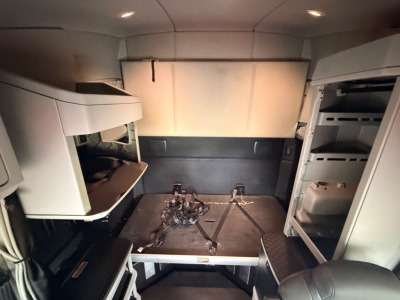 Truck cab interior showing storage compartments and exposed floor with harnesses in a Kenworth T680 crew sleeper.