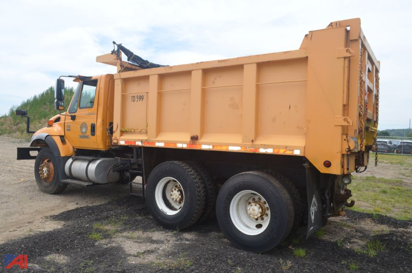 Dump truck with orange cargo bed and dual rear axles in a dirt lot, side view showing International WorkStar 7400 label and metal dump body.