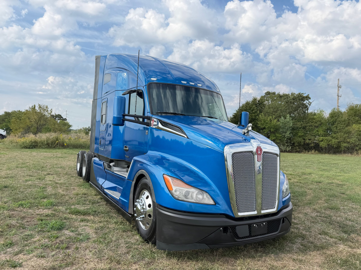 Kenworth T680 conventional sleeper truck in blue, front-left view, showing aerodynamic cab, grille, and side mirrors.