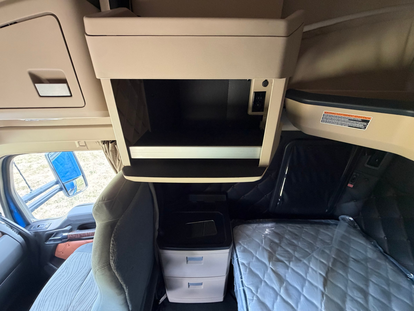 Kenworth T680 cab interior showing overhead storage unit and center console with two small drawers, and a sleeping berth with quilted mattress.