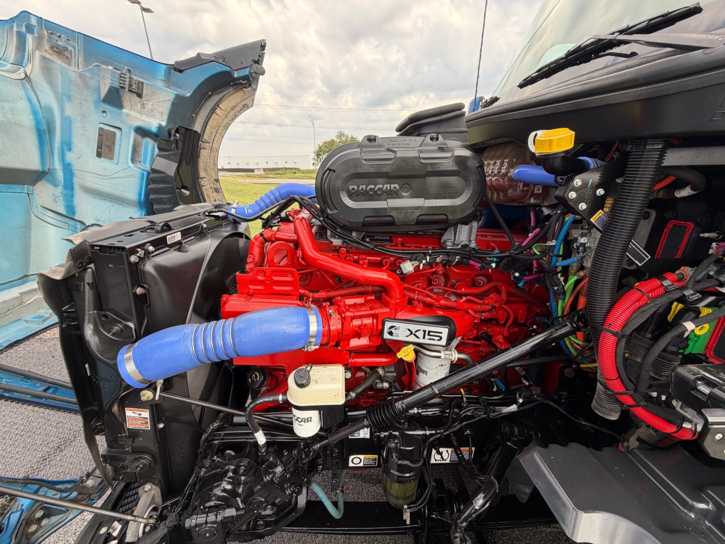 Kenworth T680 engine bay with red 6.0L? engine, blue intercooler hose, radiator, and wiring visible.