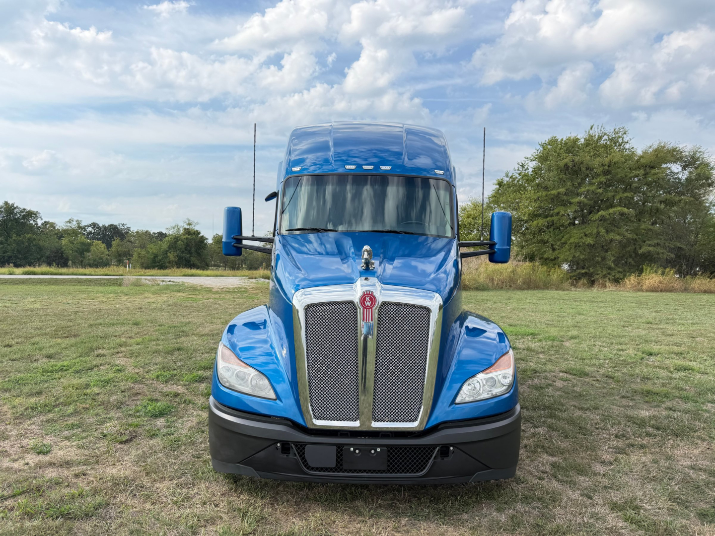 Front view of a blue 2024 Kenworth T680 conventional sleeper truck showing grille, hood, headlights, and side mirrors.
